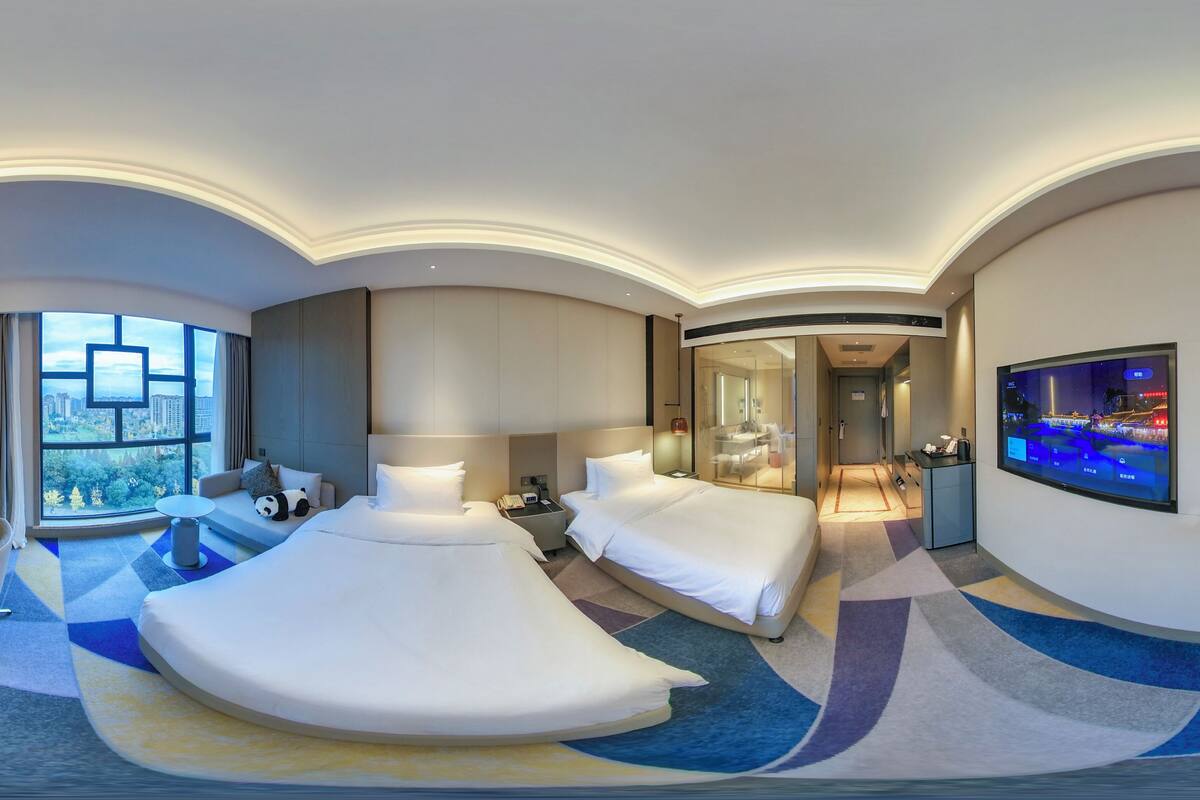 A modern hotel room with a large bed, a desk, a sofa, and a TV.