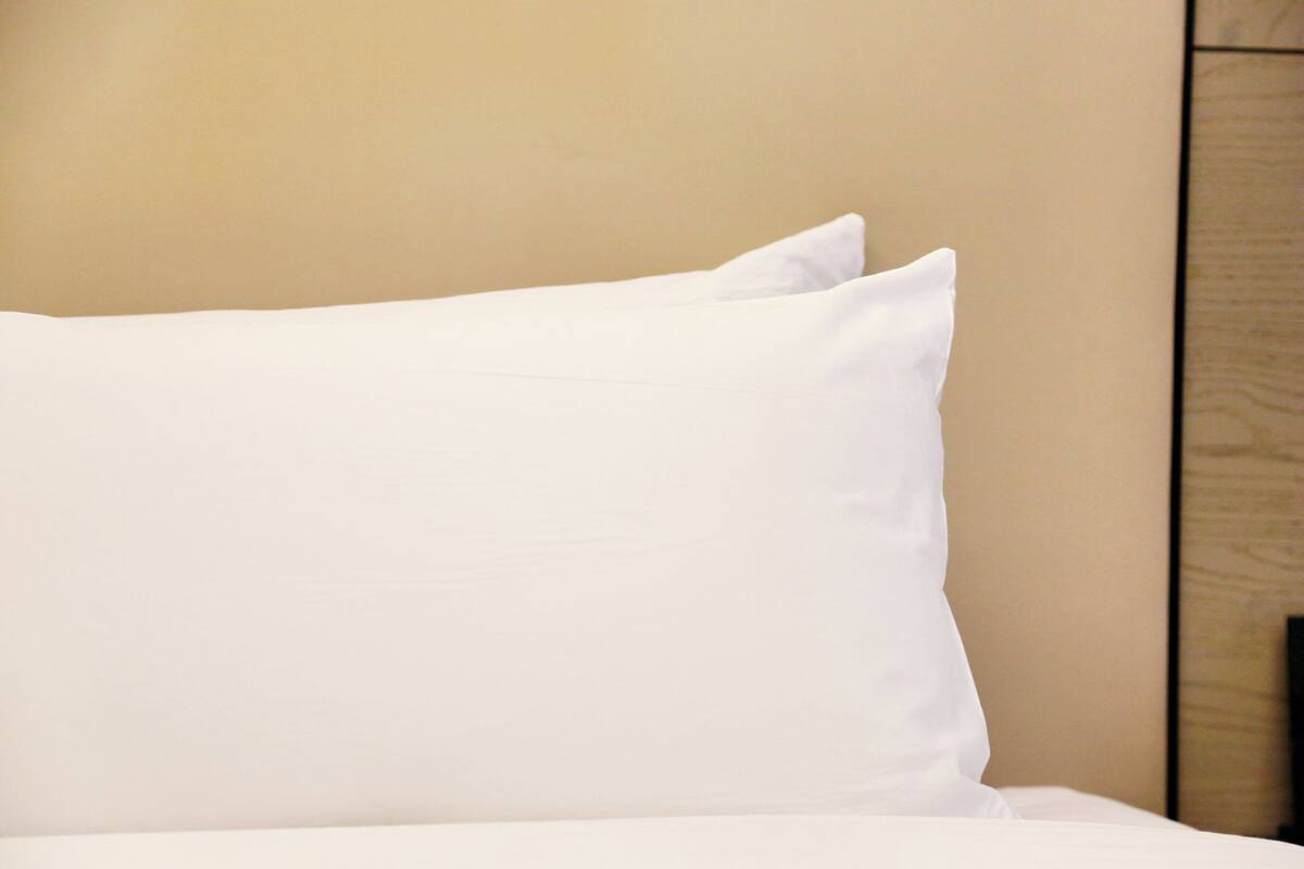 Una cama con ropa blanca y almohadas frente a una pared color beige.