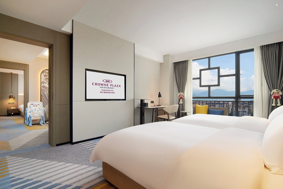 A hotel room with a large bed, a desk, and a view of the city.
