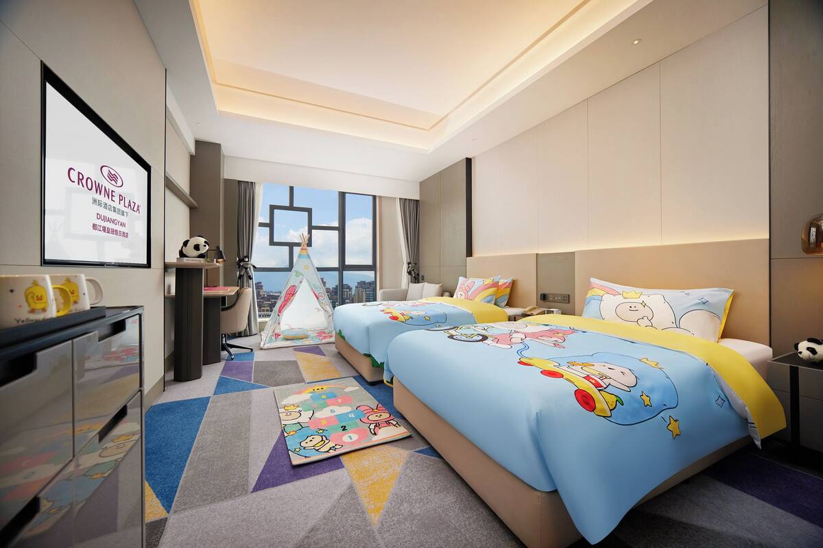 Habitación de hotel con dos camas, un escritorio, una silla, una mesita, una mesita de noche, una ventana y vistas a la ciudad.