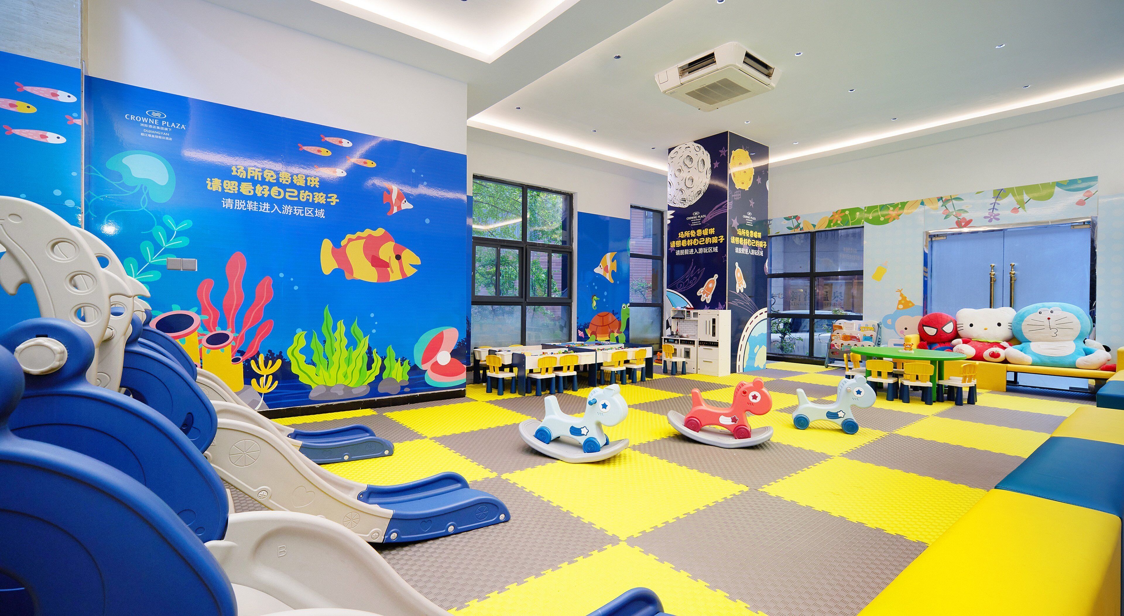 Zona de juegos infantiles con decoraciones coloridas, que incluye un tobogán, caballitos de madera y un mural con criaturas marinas.