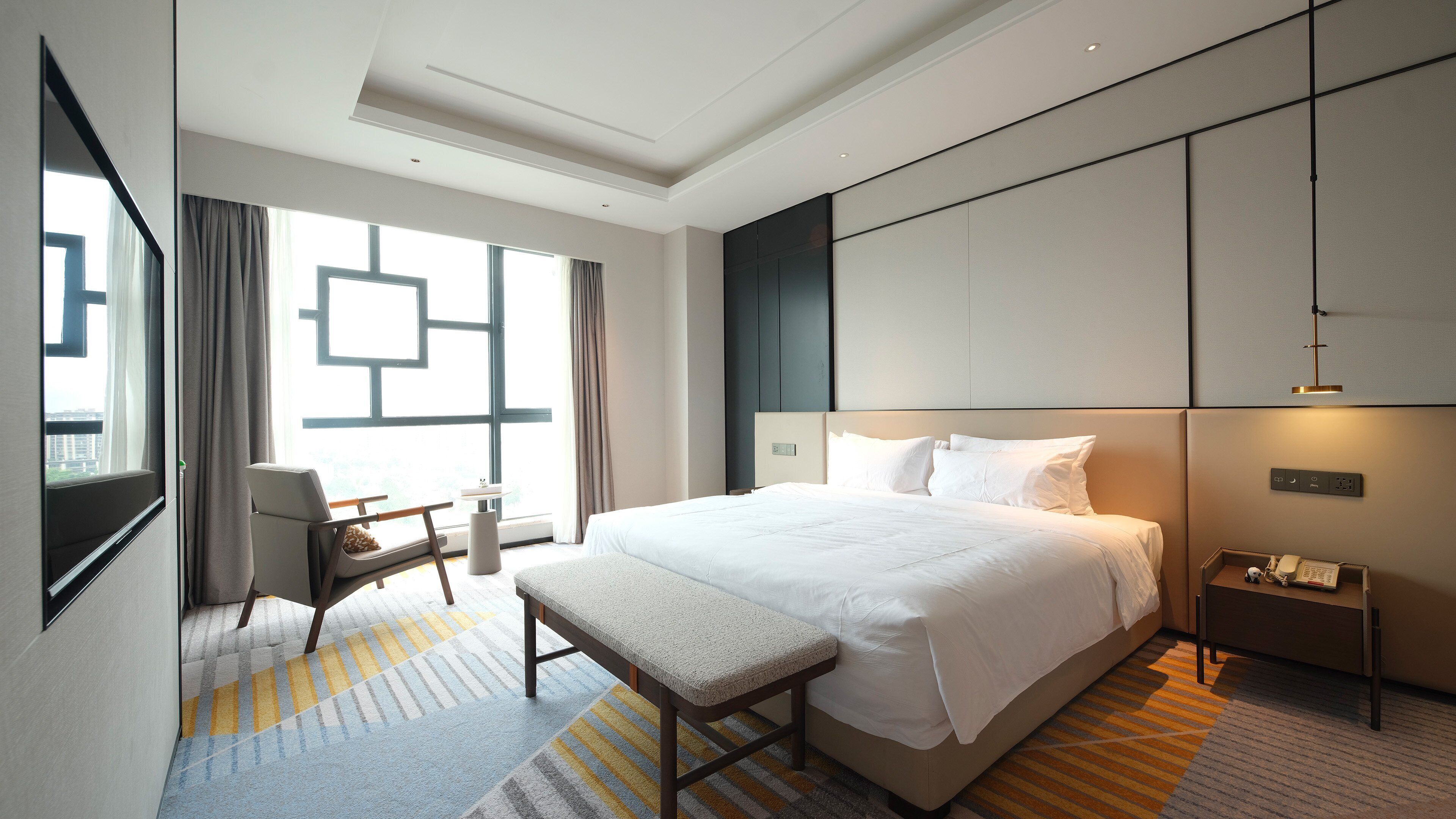 Una camera d'albergo moderna con un letto grande, una scrivania e vista sulla città attraverso ampie finestre.