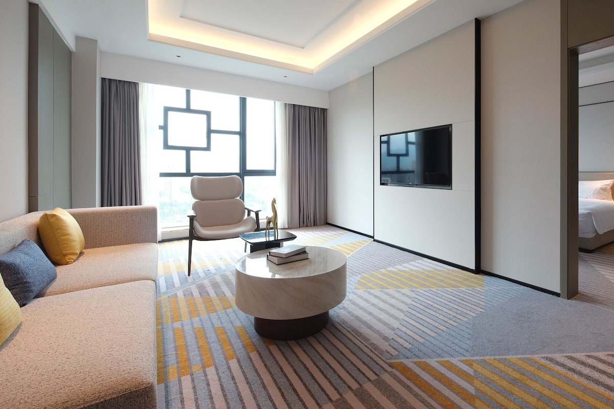 A modern hotel room with a sofa, armchair, and a round coffee table.