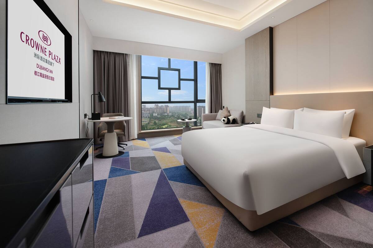 Habitación de hotel moderna con una cama grande, un escritorio, una silla y vistas a la ciudad.