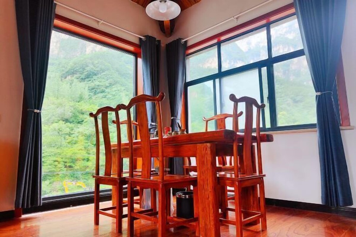 Un tavolo da pranzo in legno con sedie in una stanza con ampie finestre che offrono vista sul verde circostante.