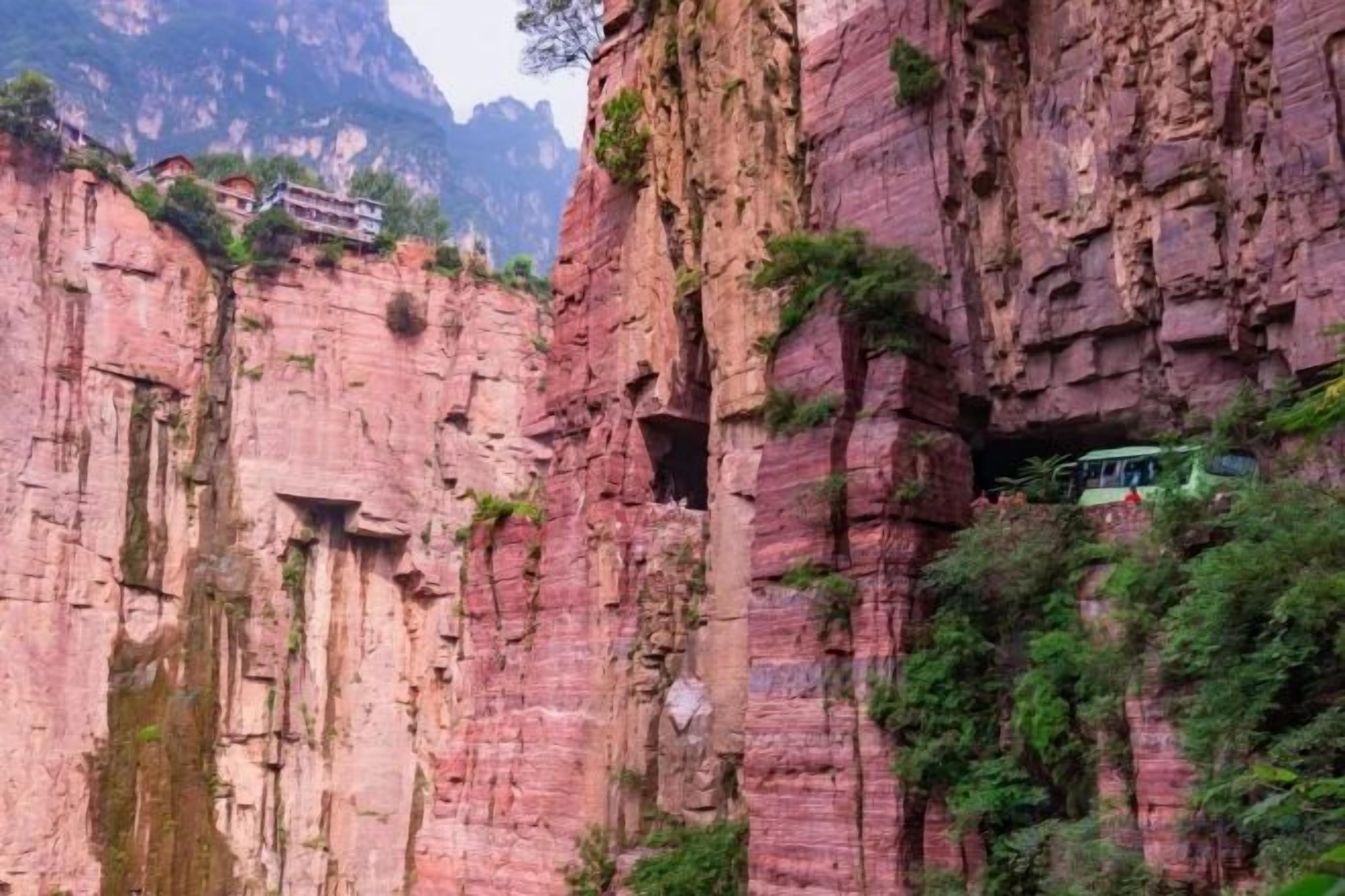 A mountain-side hotel with a rock face exterior, a narrow passageway, and a small building on top.