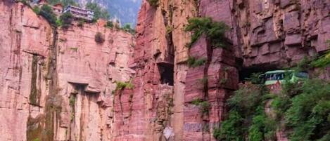 A mountain-side hotel with a rock face exterior, a narrow passageway, and a small building on top.