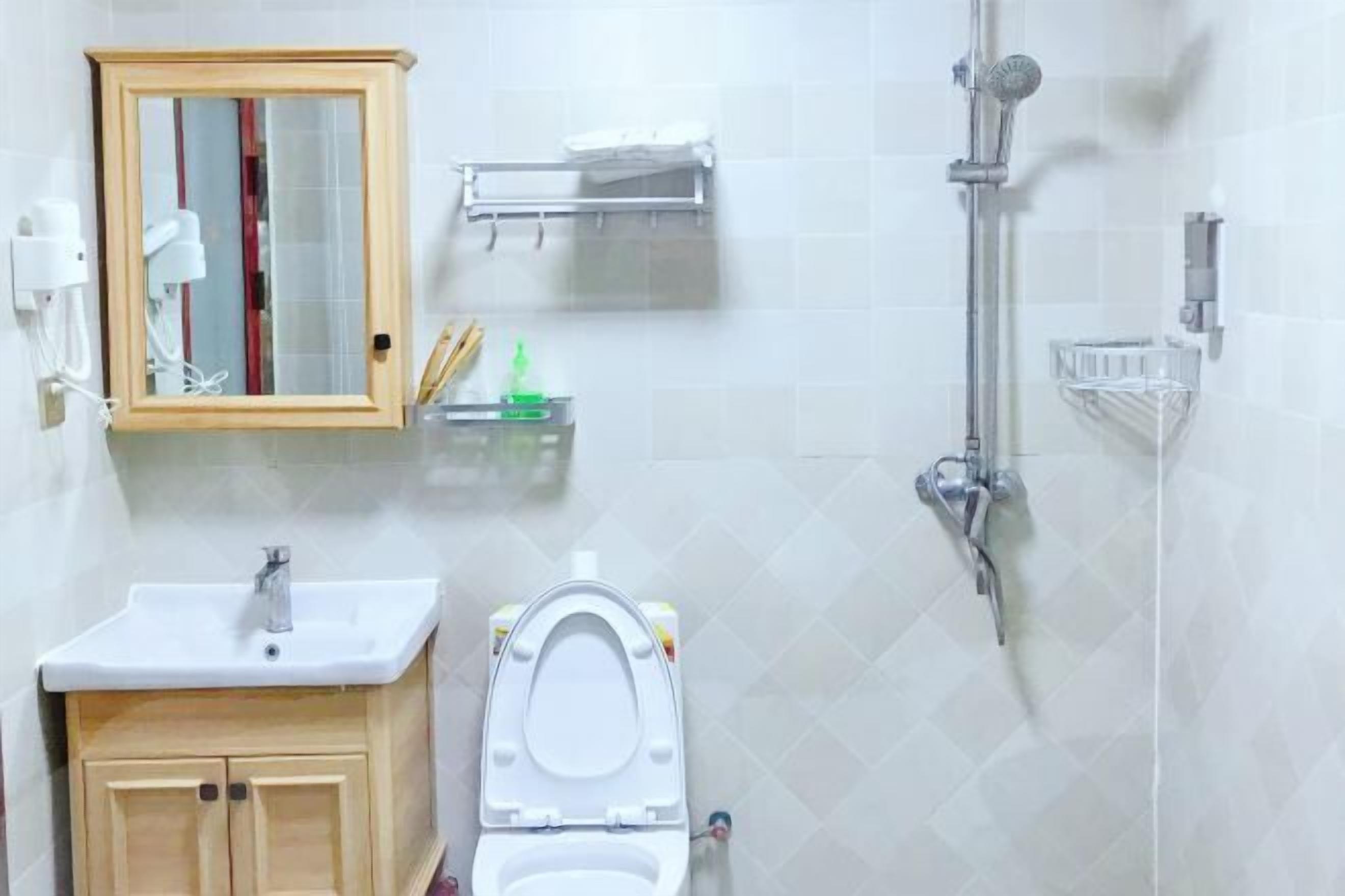 A bathroom with a wooden cabinet, a white sink, a toilet, a mirror, and a shower.