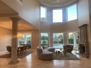 Relax in a spacious living area with a high ceiling and large windows offering a view of the outdoors.