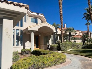 Stucco and tile facade with a charming entrance, surrounded by manicured gardens and palm trees.