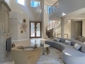 Relax in this elegantly designed living area with a grand staircase, comfortable seating, and a fireplace.