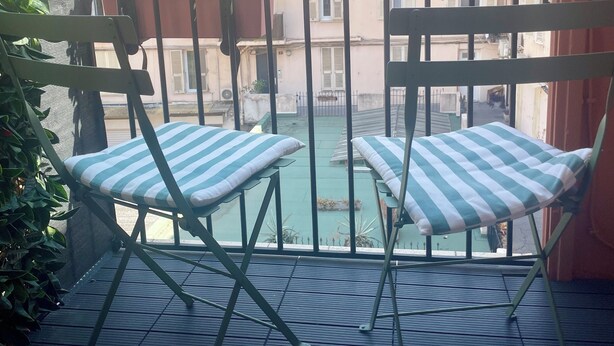 A balcony with two striped chairs and a table, overlooking a courtyard with buildings in the background. - One minute from Place Masséna,  fully equipped STUDIO with balcony (Nice)