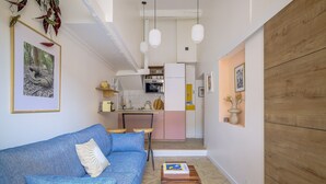 A compact living space with a blue sofa, a small wooden table, and a kitchenette in the background. - One minute from Place Masséna,  fully equipped STUDIO with balcony (Nice)