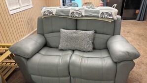 A grey leather sofa with a patterned pillow and a decorative throw blanket.