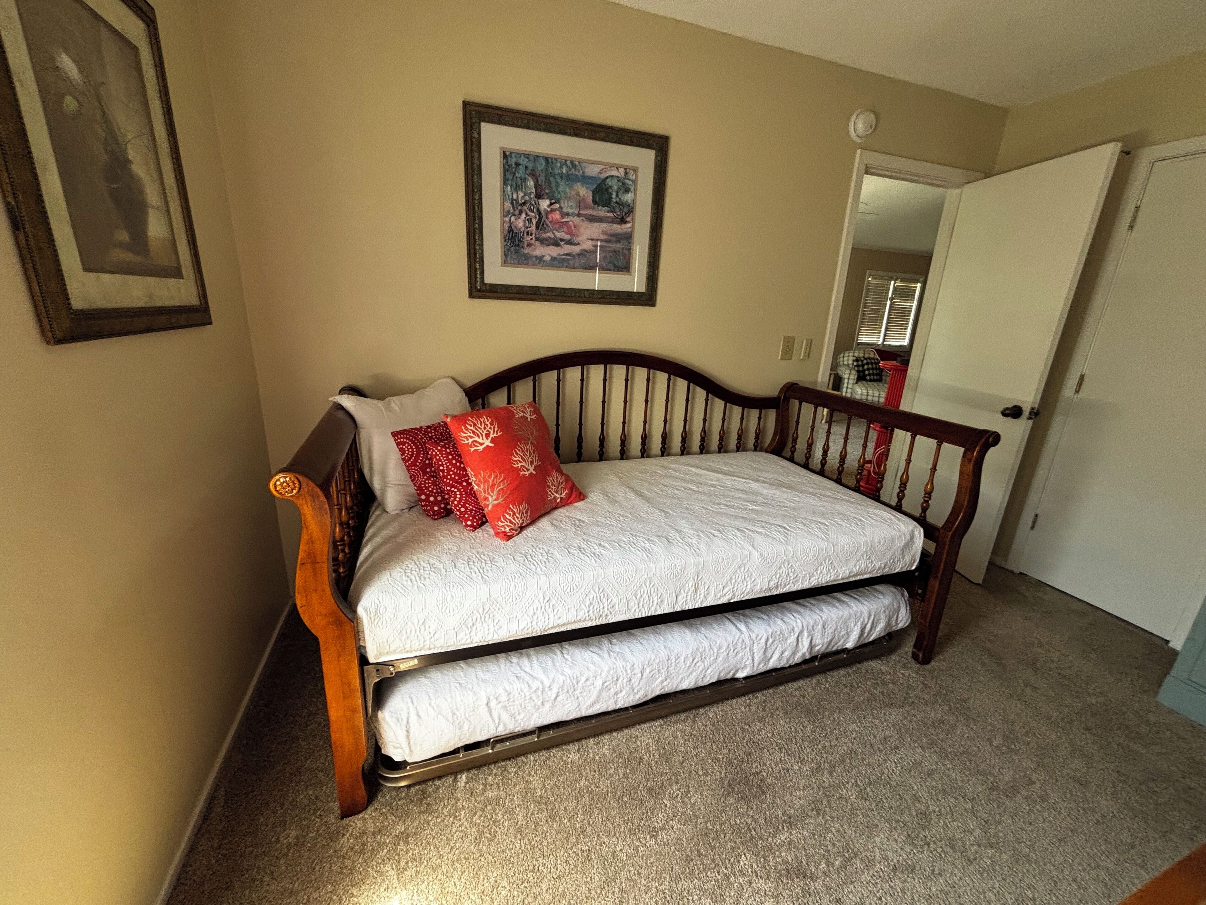 A bedroom with a double bed, a wooden headboard, a framed picture on the wall, and a door to the right.
