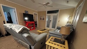 A living room with a grey sofa, a blue armchair, a wooden coffee table, and a TV on a stand.