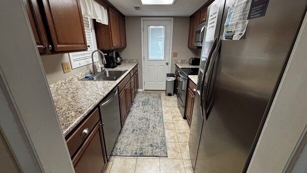 A compact kitchen with wooden cabinets, stainless steel appliances, and a tiled floor.