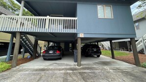A two-story house with a balcony, two cars parked under the structure, and a visible address number '3'.
