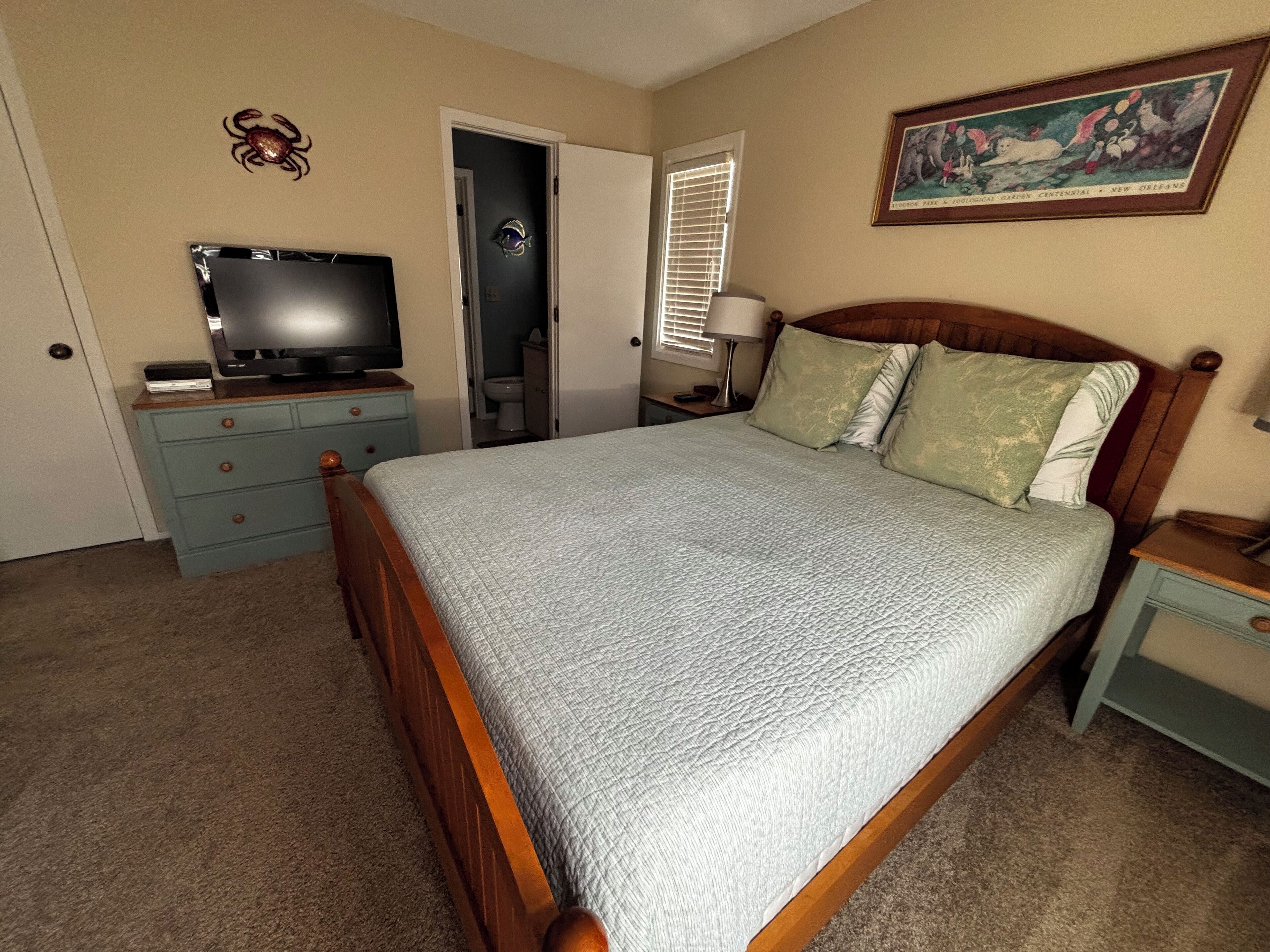 A bedroom with a bed, a dresser, a television, and a painting on the wall.