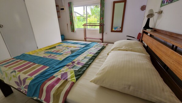 A bedroom with a bed, a wooden headboard, a window with curtains, a mirror, and a bedside lamp.