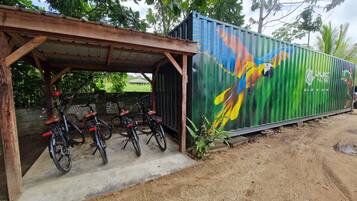 Un espacio cubierto para estacionar bicicletas con un mural de un ave sobre un contenedor verde.