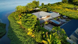 Une maison avec un toit en métal, entourée d’une végétation luxuriante et bordée par un plan d’eau.