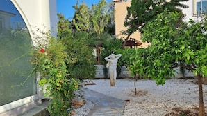 Un jardin agrémenté d’une statue, d’un chemin de gravier et de différentes plantes.