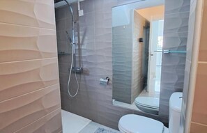 Un baño moderno con cabina de ducha de cristal, un inodoro y una bañera.
