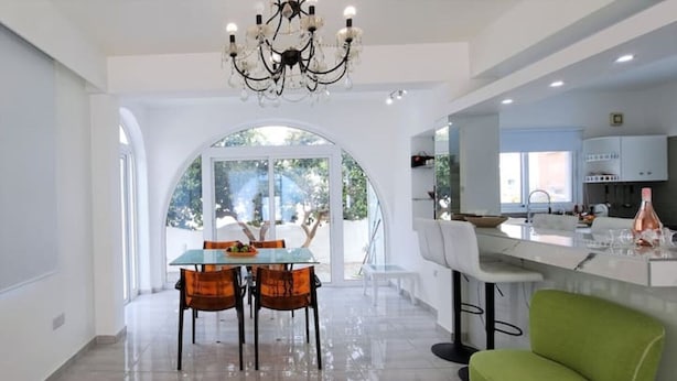 Une cuisine moderne avec des meubles blancs, un coin bar et un espace repas agrémenté d’une table et de chaises en verre.