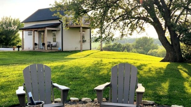 A house with a covered porch and a fire pit area with two Adirondack chairs and a table set for a meal.
