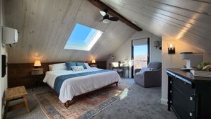 A bedroom with a skylight, a bed, a desk, a chair, and a dresser.