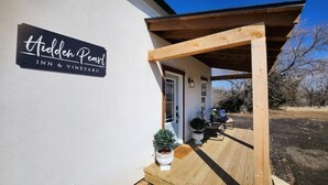 A sign for Hidden Pearl Inn & Vineyard, a covered wooden porch, and potted plants.