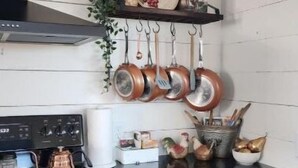 A kitchen with a black stove, wooden cabinets, and copper pots hanging on hooks.