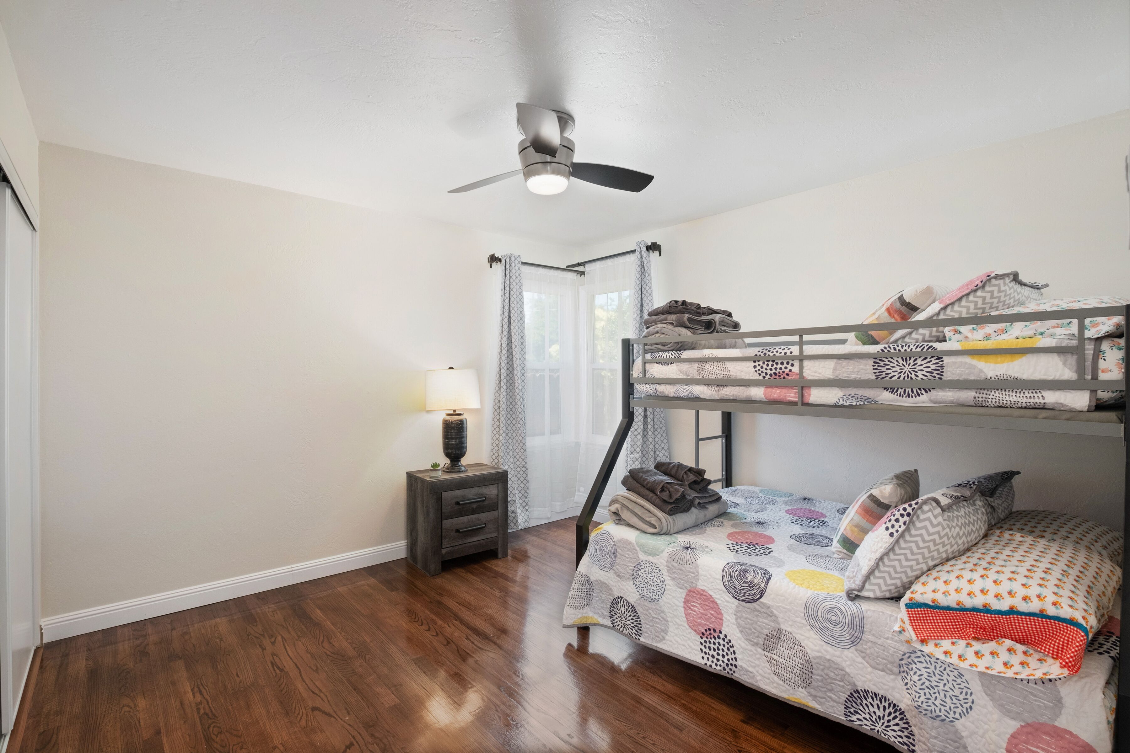 A room with a bunk bed, a nightstand with a lamp, and a ceiling fan.