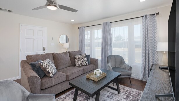 A living room with a sofa, armchair, coffee table, and a ceiling fan.