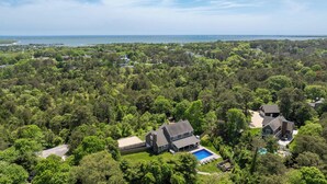 Une vue aérienne d’un quartier résidentiel, avec des maisons entourées d’une végétation luxuriante, une grande piscine et, au loin, une vue sur la mer.