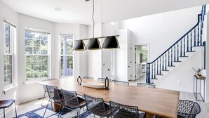 Un vaste espace dédié à la salle à manger, avec une longue table en bois, des chaises en métal noir ajouré et un luminaire suspendu au design moderne.