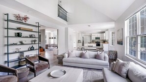 Un vaste espace de vie comprenant un canapé blanc, une table basse et une étagère en verre où sont disposés des objets décoratifs.