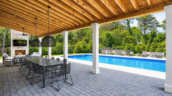 An outdoor patio with a pool, a stone fireplace, and outdoor furniture.