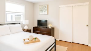 Een keurig opgemaakt slaapkamer met een bed, nachtkastje, televisie en een kledingkast.