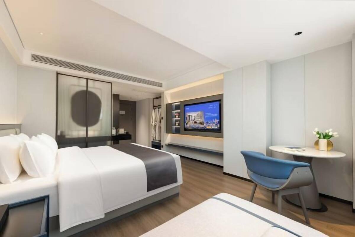 A modern hotel room with a bed, a TV, a desk, and a chair.