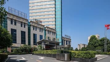 A modern hotel with a prominent glass facade, a well-maintained entrance area with directional arrows, and a flagpole with a flag.
