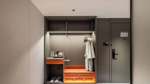 Une chambre d’hôtel compacte comprenant un banc intégré, une petite coiffeuse avec des articles de toilette et une armoire avec un peignoir.