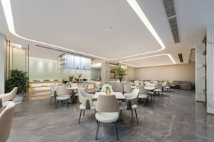 Un comedor moderno con mesas y sillas, una cocina al fondo y un diseño limpio y contemporáneo.