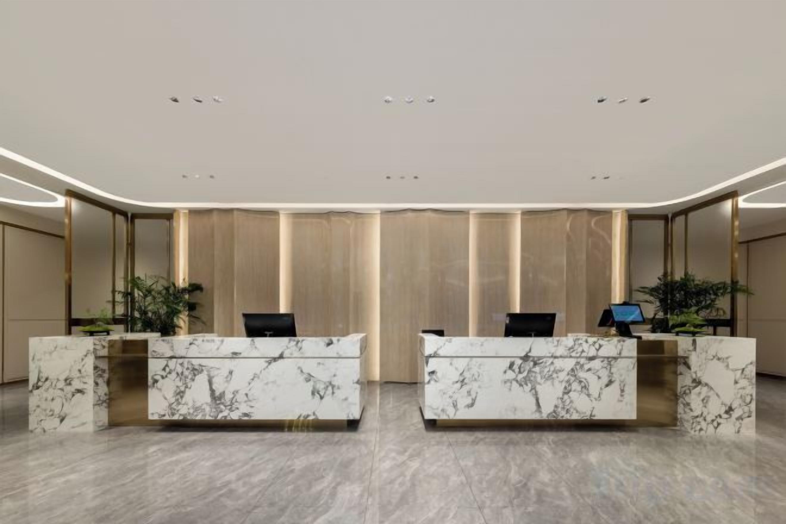 A reception area with marble reception desks, a modern ceiling design, and a large mirror.