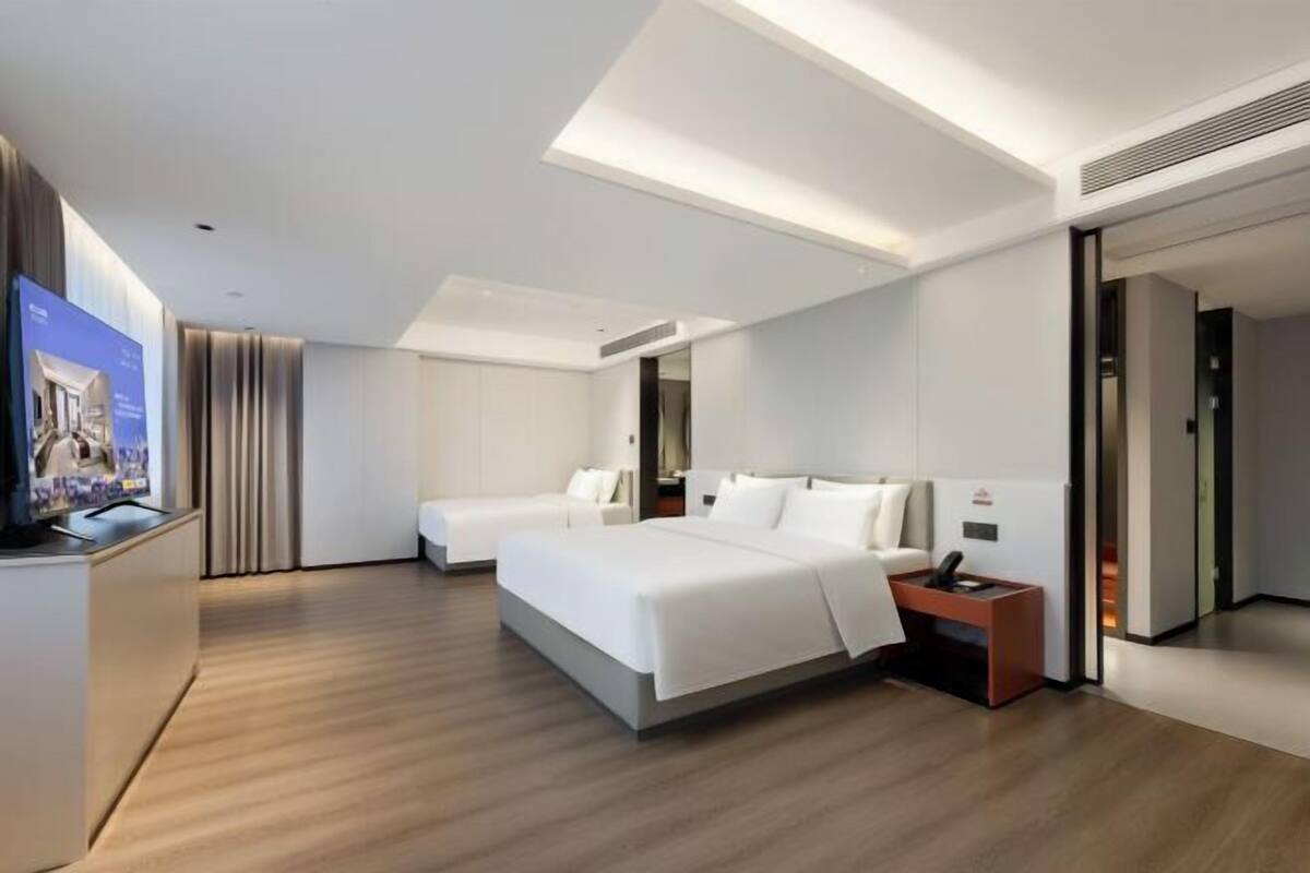 A modern hotel room with a large bed, a bedside table, a TV, and a wardrobe.