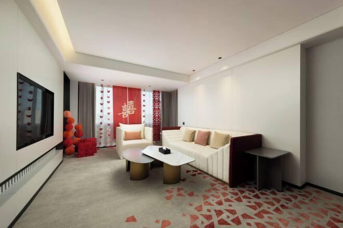 A modern hotel room with a white sofa, a small coffee table, a TV, and a patterned carpet.