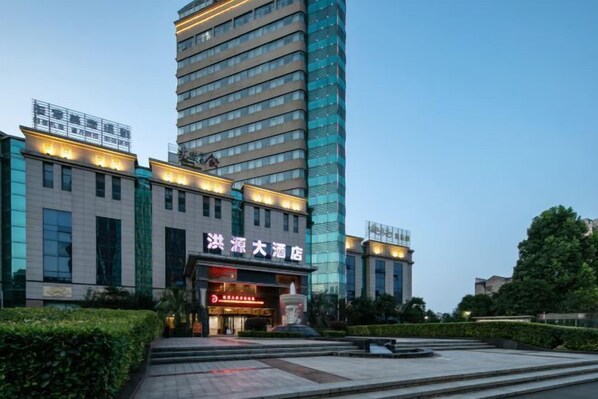 A hotel with a modern glass facade, a prominent entrance with illuminated signage, and a landscaped courtyard. - Hongyuan Hotel (Gucheng)
