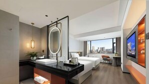 Une chambre d’hôtel moderne dotée d’un grand lit, d’un coin salon séparé, d’une salle de bain avec un meuble-lavabo et d’une vue sur la ville.