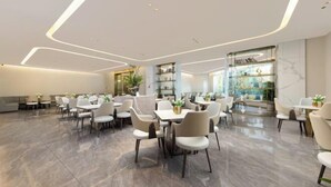 Un espace de restauration spacieux et moderne, avec des tables et des chaises blanches, un sol en marbre et un mur de verre orné d’œuvres d’art.